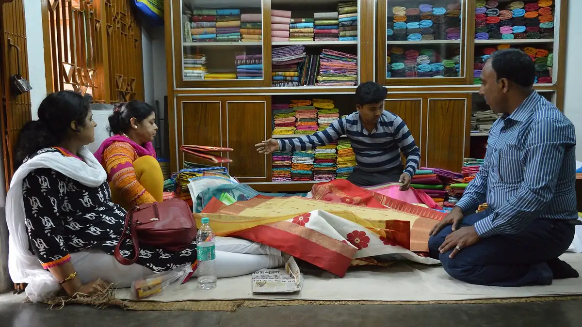 A shopkeeper showing tussore sarees to customers seated on the shop floor