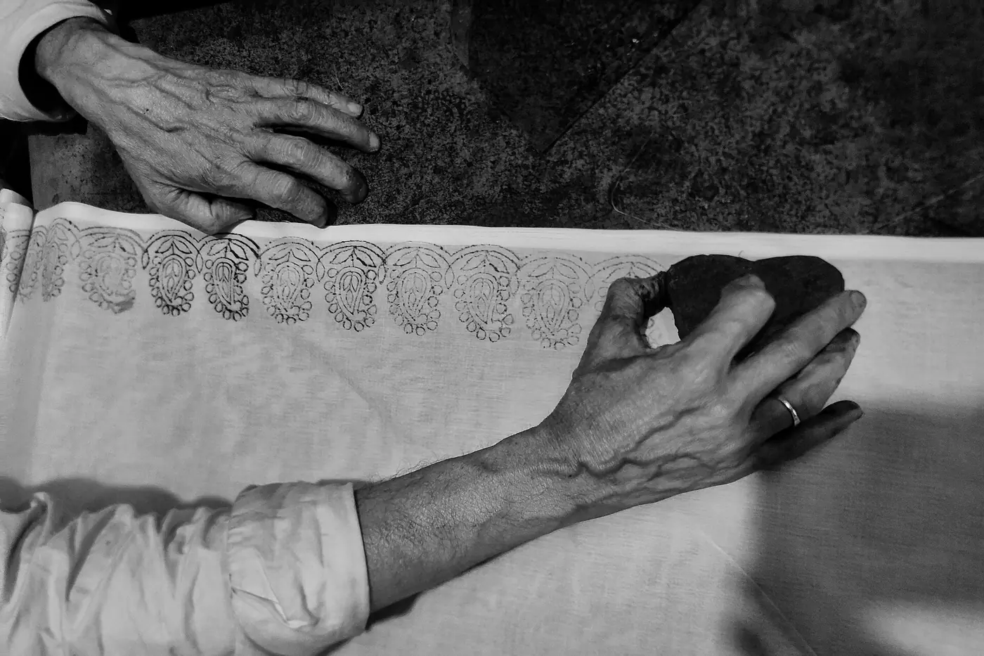Hands pressing a wooden block onto cloth in black and white